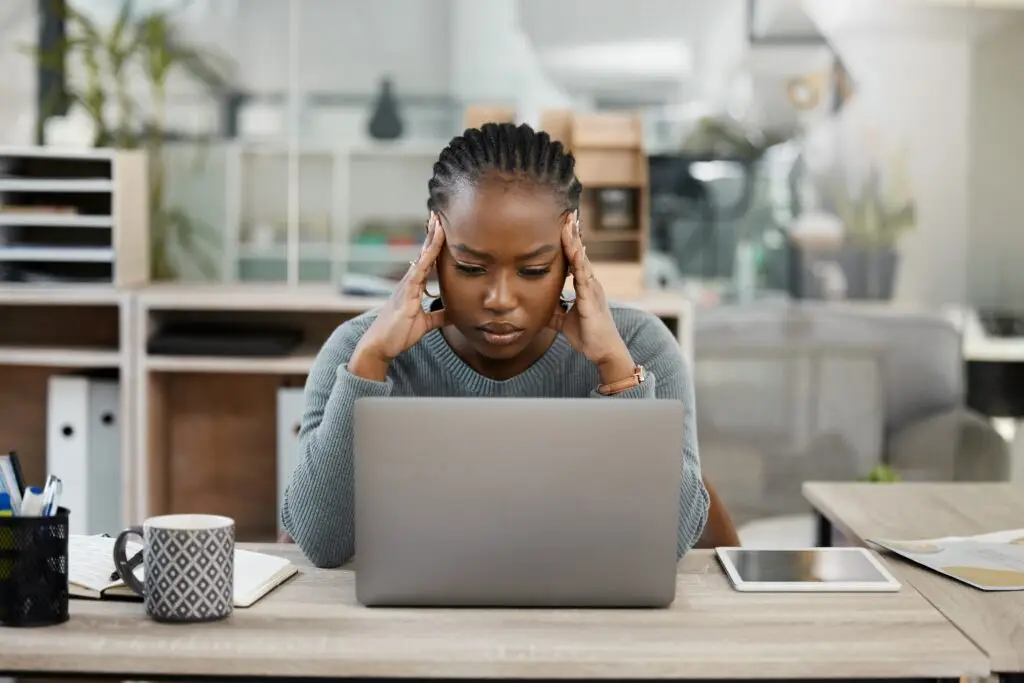Female office worker looking at laptop with both hands over the side of her head in headache frustration motion.