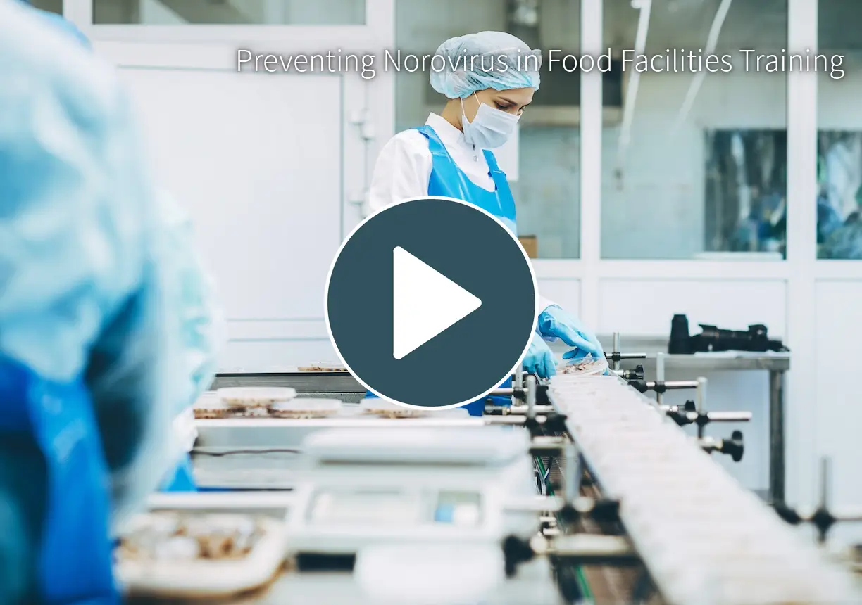 **Short Alt Text:** A food processing worker wearing a blue apron, protective hairnet, face mask, and gloves inspects packaged items on a conveyer belt in a clean industrial facility. **Detailed Alt Text:** A side view of a food production worker standing at a processing line in a clean, brightly lit facility. The worker is wearing a white lab coat, a bright blue waterproof apron, blue gloves, a hairnet, protective eyewear, and a surgical face mask. She is carefully handling small, clear plastic containers filled with food as they move along a conveyor belt system equipped with a digital scale.